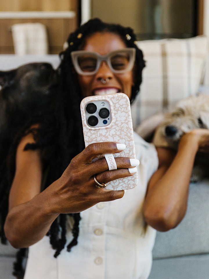  A woman holding a Beige Blossoms Loopy Case while taking a selfie.|| feature-media