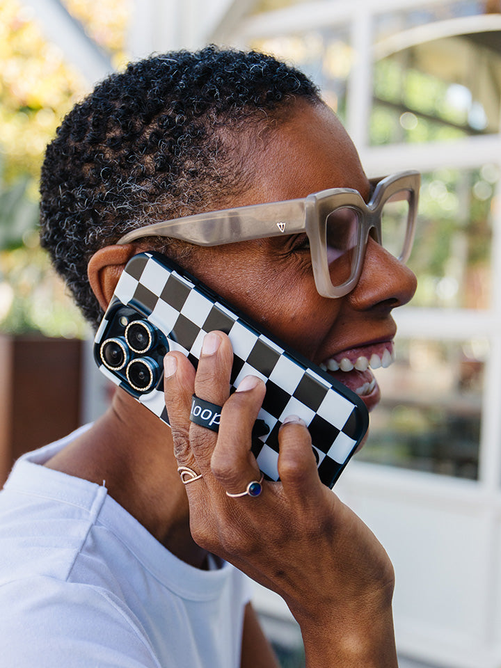 A woman talking on the phone while holding a Black and White Checkered Loopy Case. || feature-media