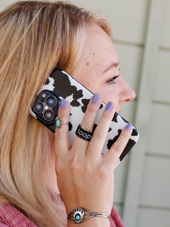 A woman talking on the phone while holding a Cow Print Loopy Case.|| feature-media