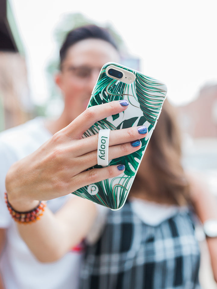 A woman taking a selfie while holding a Monstera Loopy Case. || feature-media