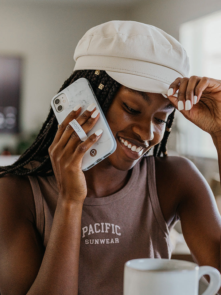 A woman talking on the phone while holding a White Marble Loopy Case. || feature-media