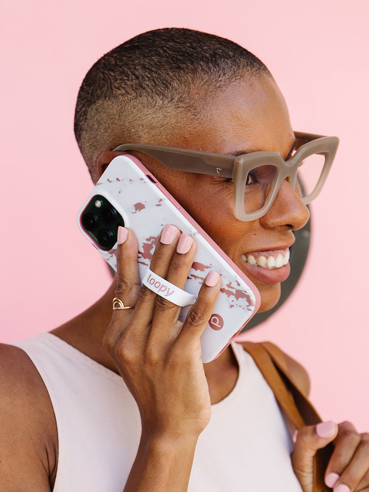 A woman talking on the phone while holding a Rose Marble Metallic Loopy Case.|| feature-media