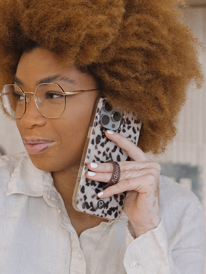 A woman talking on the phone while using a Blonde Tortoise Loopy Case. || feature-media